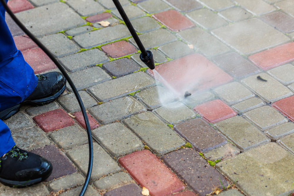 A pressure washer lance clearing moss from block paving joints